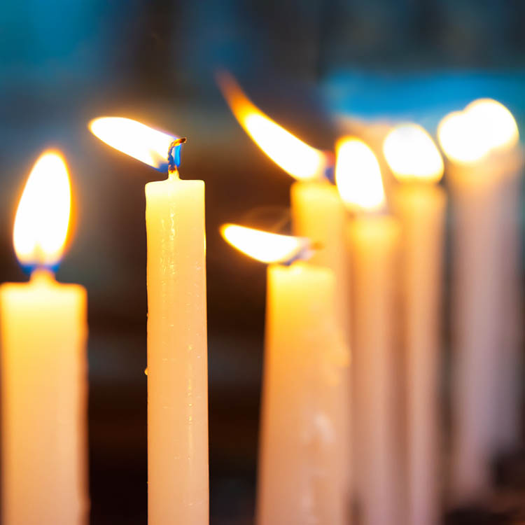 Close-up of several lit white candles burning with warm orange flames.