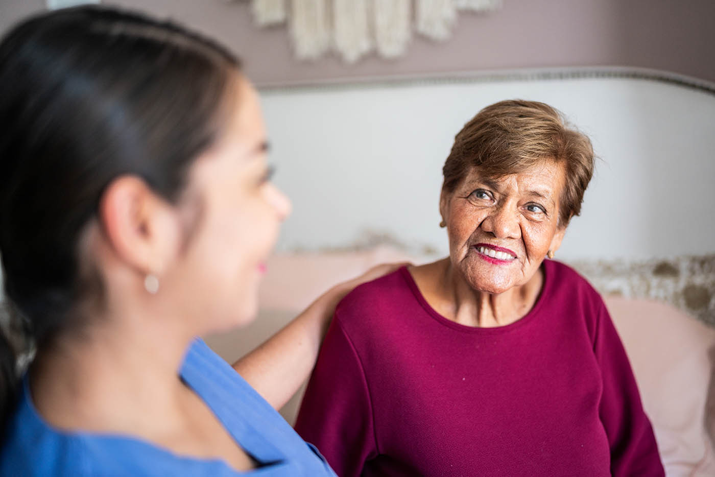 An aide places a supportive hand on an older woman's shoulder as they sit together.